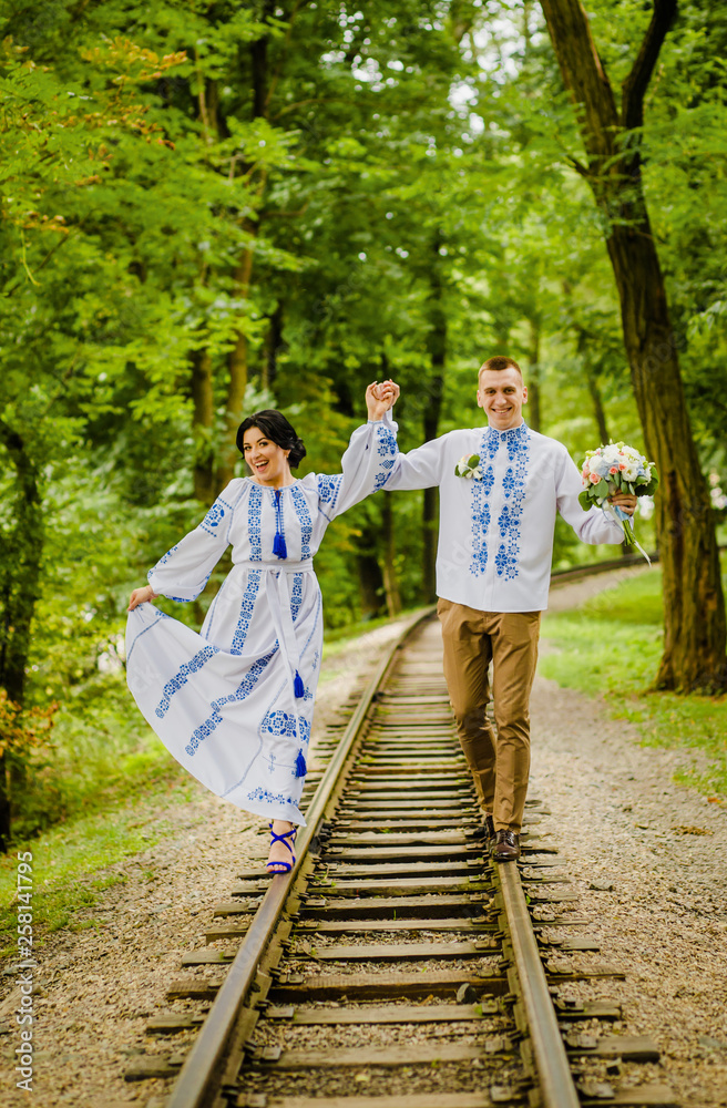 Fototapeta premium Happy couple in ethnic clothes going along the track holding hands