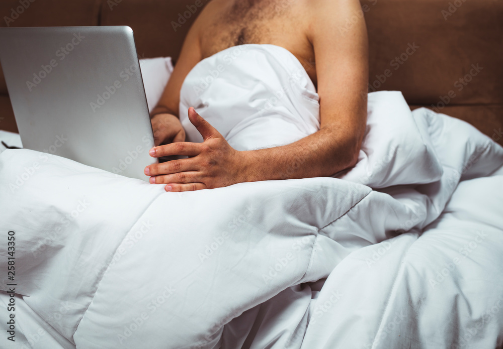 Young man is sitting in bed and watching movie on laptop Young man is sitting in bed and watching movie on laptop