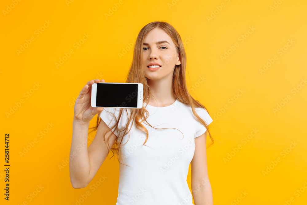 Portrait of a beautiful girl , showing a blank screen phone on a yellow background