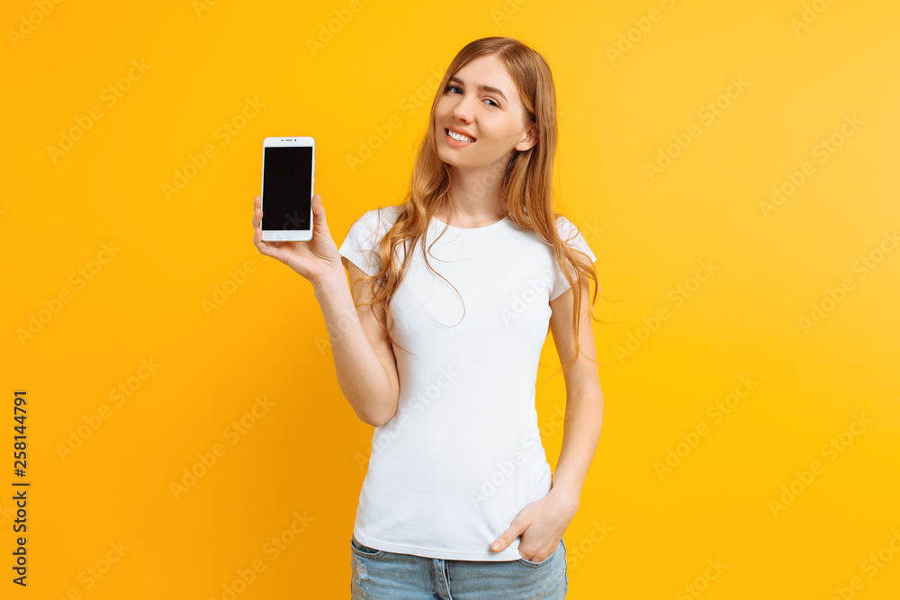 Portrait of a beautiful girl , showing a blank screen phone on a yellow background
