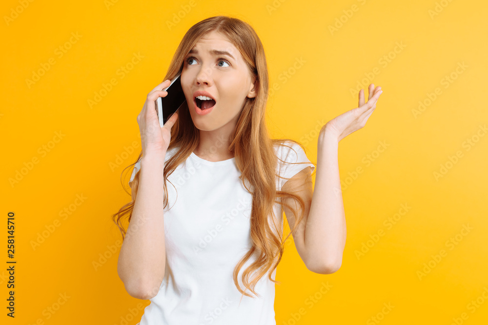 Irritated and uncertain girl talking on the phone, on a yellow background Irritated and uncertain girl talking on the phone, on a yellow background