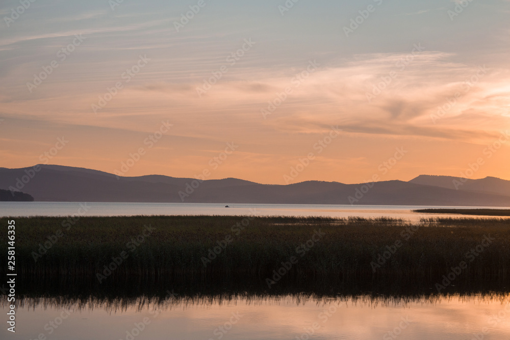 Grass on river, sunset landscape. Beautiful mountains and sky. Clouds
