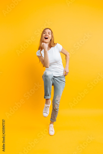 Full length, enthusiastic girl , celebrating success on a yellow background