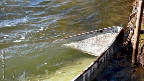 Flooded boat on the shore of the pond. Waves run on the boat.