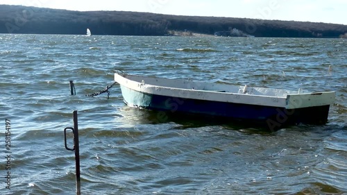 Boat on a leash on the shore of the city pond. Away windsurfing