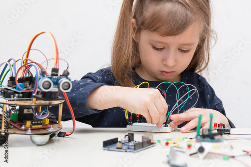 A cute girl constructs metal robot and program it. The boards and microcontrollers are on the table. STEM education inscription. Programming. Mathematics. The science. Technologie. DIY. 