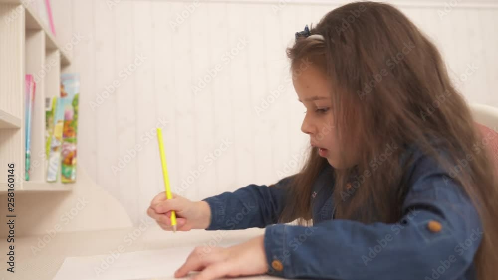 Little cute girl sits at the table and draws with yellow pencil. Little cute girl sits at the table and draws with yellow pencil.