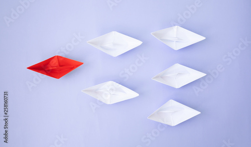 Leadership concept. Red leader paper ship leading among white on blue background.