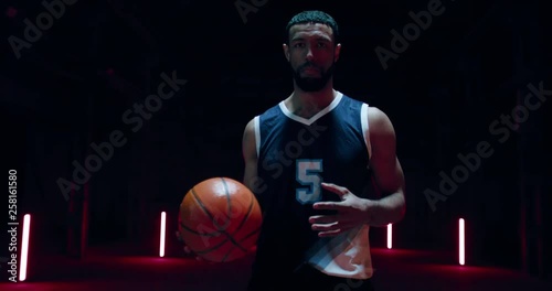 HANDHELD African American professional basketball player posing with a ball against dark background in a large abandoned warehouse. 4K UHD 60 FPS SLOW MOTION photo