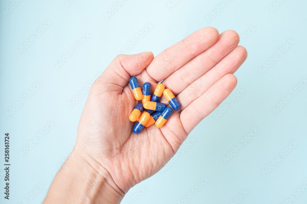 Close-up shot of a hand holding color pills on blue background. Close-up shot of a hand holding color pills on blue background.