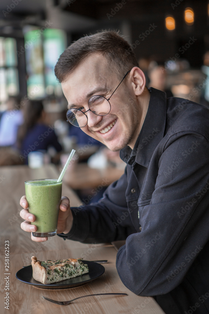 Side view of a smliling businessman talking on a phone while sitting in cafe, drink smoothy, eat pie Side view of a smliling businessman talking on a phone while sitting in cafe, drink smoothy, eat pie