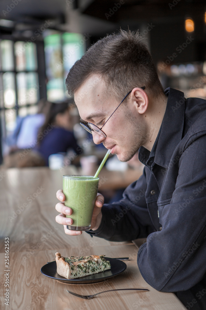 Young stylish man enjoys a cake and a drink while sitting in a cafe with large windows Young stylish man enjoys a cake and a drink while sitting in a cafe with large windows