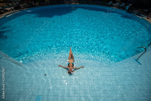 Over head rear view of an attractive young woman swimming under water and wearing in bikini