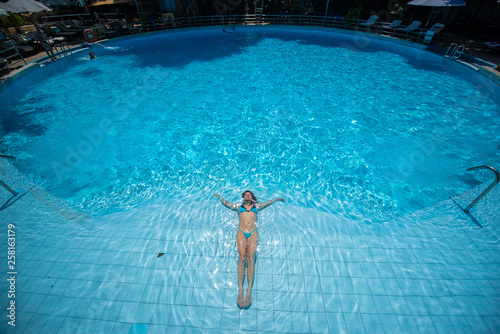 Over head rear view of an attractive young woman swimming under water and wearing in bikini