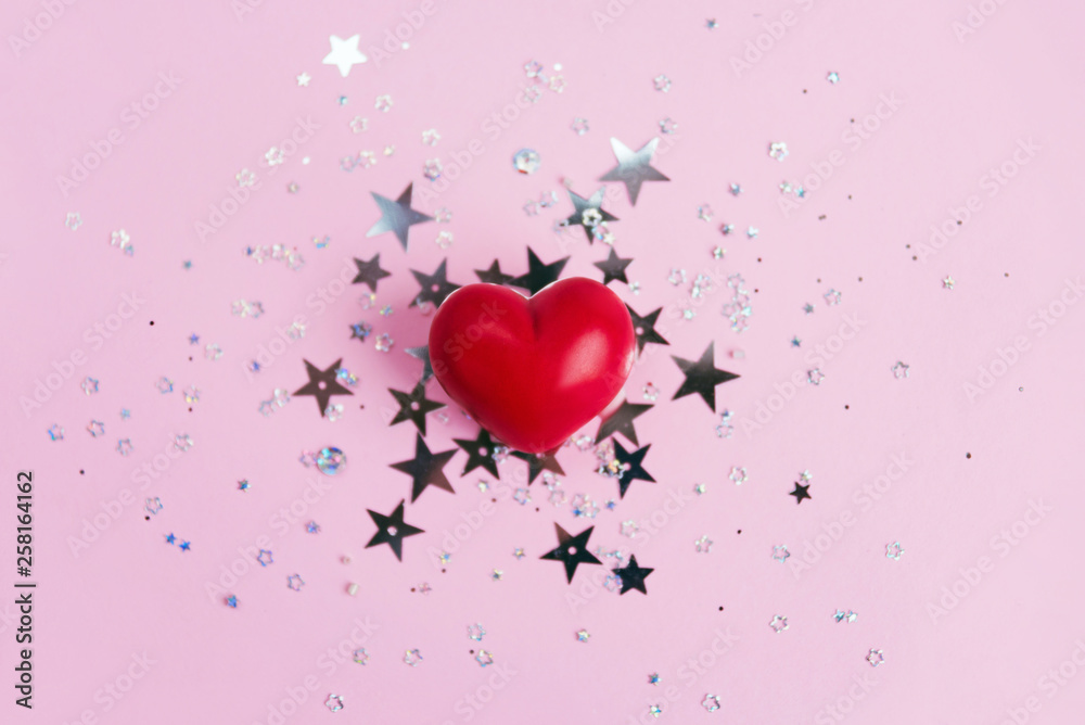 Red heart on pink background with star glitter confetti.