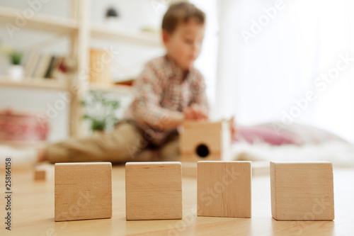 Little child sitting on the floor. Pretty boy palying with wooden cubes at home. Conceptual image with copy or negative space and mock-up for your text