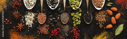 A variety of spices, seeds, nuts in spoons on a dark rustic background. Top view, flat lay.