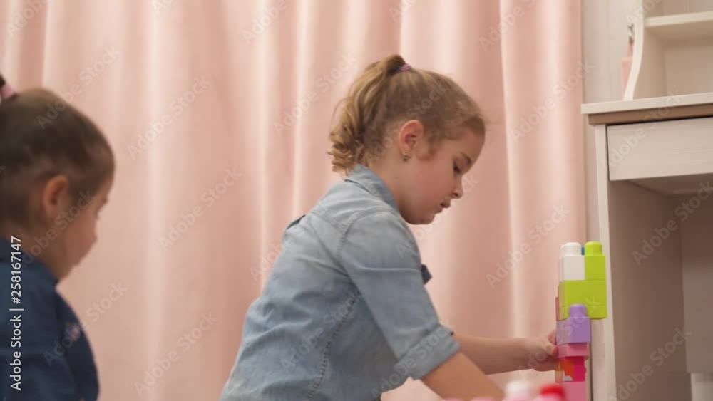 Little girls build a multicolored toy tower in a bright room Little girls build a multicolored toy tower in a bright room