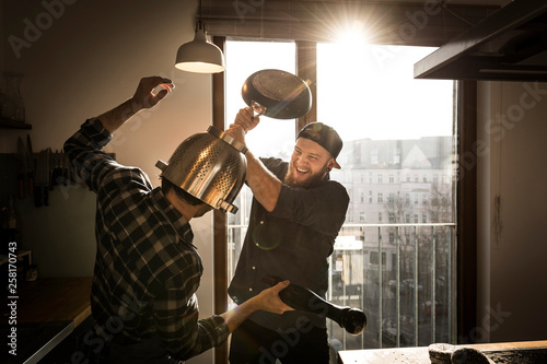 Friends having a duel with a colander and a pan in the kitchen photo