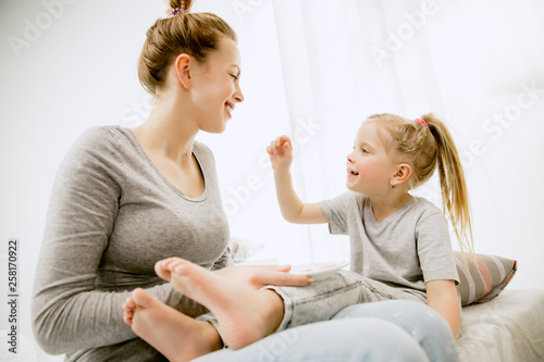 Young mother and her little daughter at home at sunny morning. Soft pastel colors. Happy family time on weekend. Mother's Day concept. Family, love, lifestyle, motherhood and tender moments concepts.