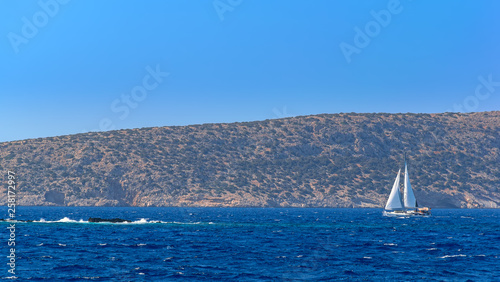 White sailing yacht ride on pure azure blue bay water along of rocky coastline of Rhodes island, Greece.