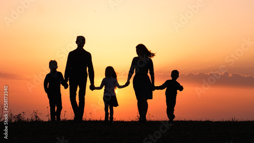 Silhouettes of happy family holding the hands in the meadow during sunset.