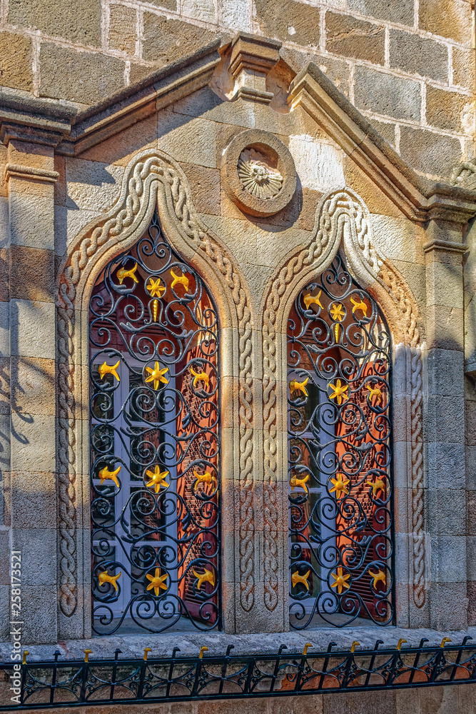 Close-up view of an ancient window with ornate decorated metal bars in an old limestone fortification wall.