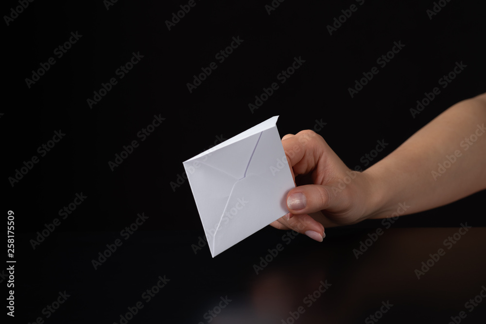 white envelope in a female hand on black background white envelope in a female hand on black background