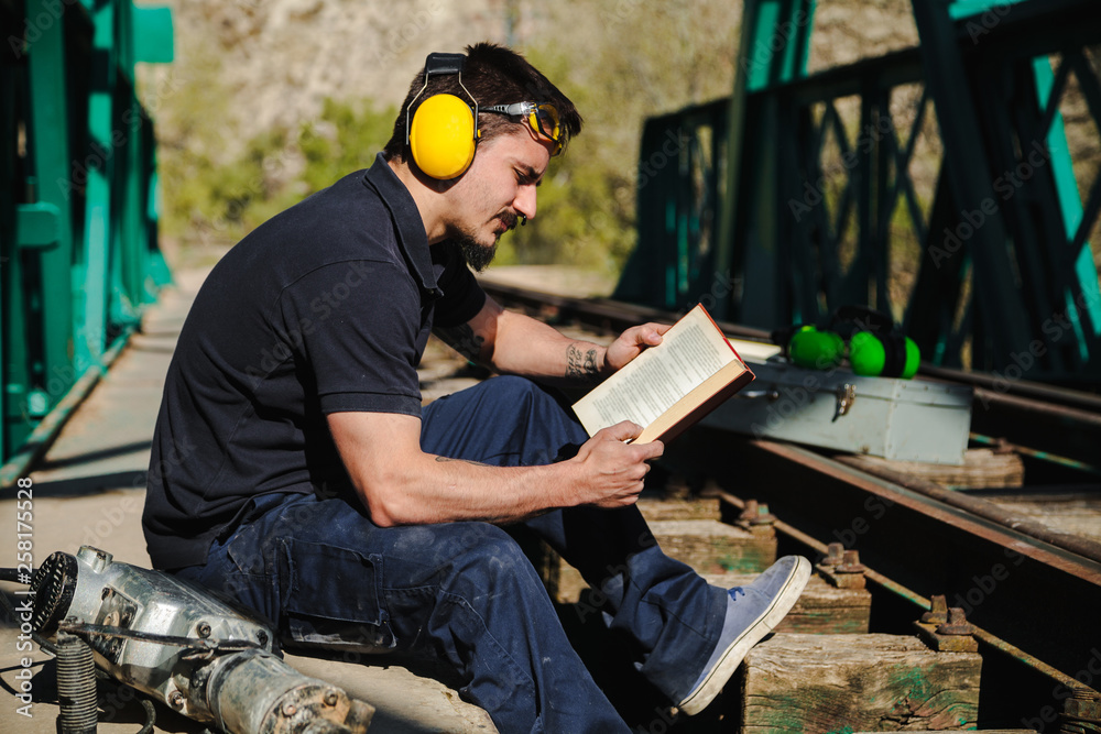 Young construction worker reading a book on old railway bridge