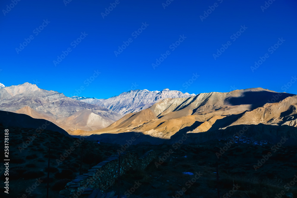 View on Himalayas from Annapurna Circuit Trek, Nepal. Early morning in the mountains. Pathway covered in shadow, high mountains peaks catching the first beams of sunlight. Multicolored mountains.