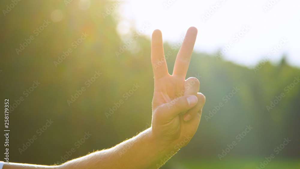 LENS FLARE, DOF: Bright sunbeams shine on male hand and showing the peace sign. LENS FLARE, DOF: Bright sunbeams shine on male hand and showing the peace sign.