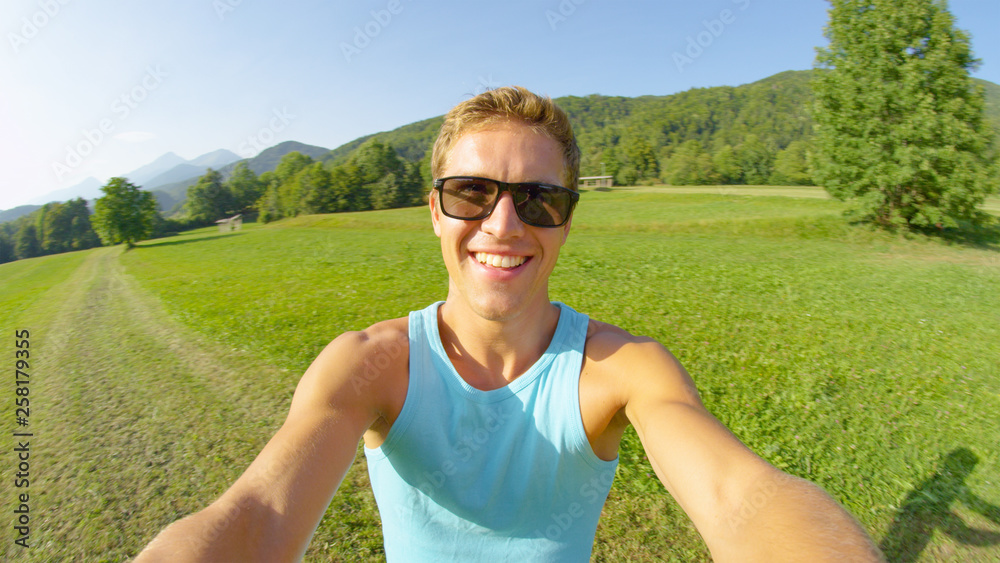 SELFIE: Handsome young man wearing sunglasses spins around the sunny meadow.