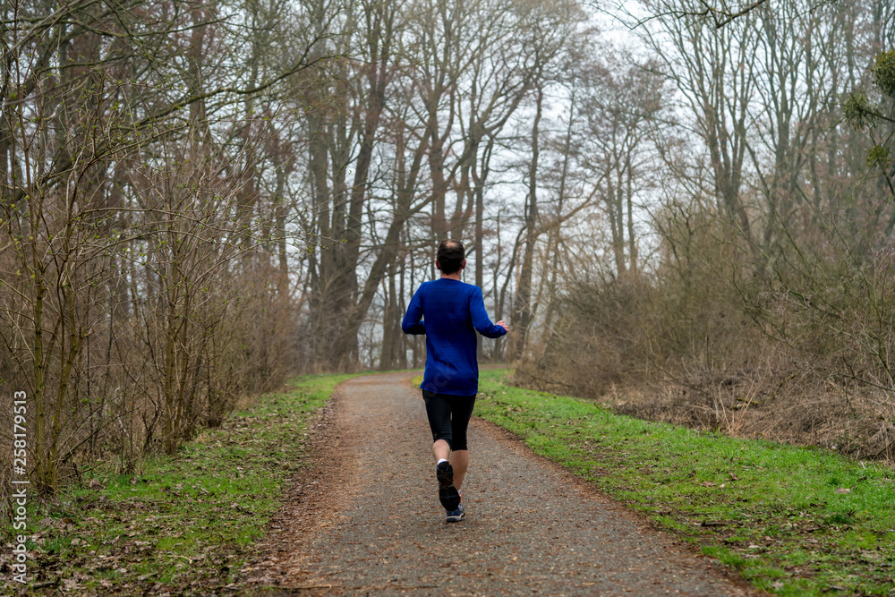 Ultramarathon runner running along a forest path in early spring Ultramarathon runner running along a forest path in early spring