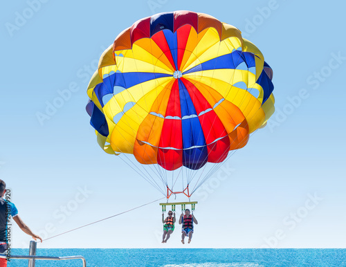 Happy smiling couple Parasailing on Tropical Beach in summer. Newlyweds under parachute hanging mid air. Having fun. Tropical Paradise. Positive human emotions.