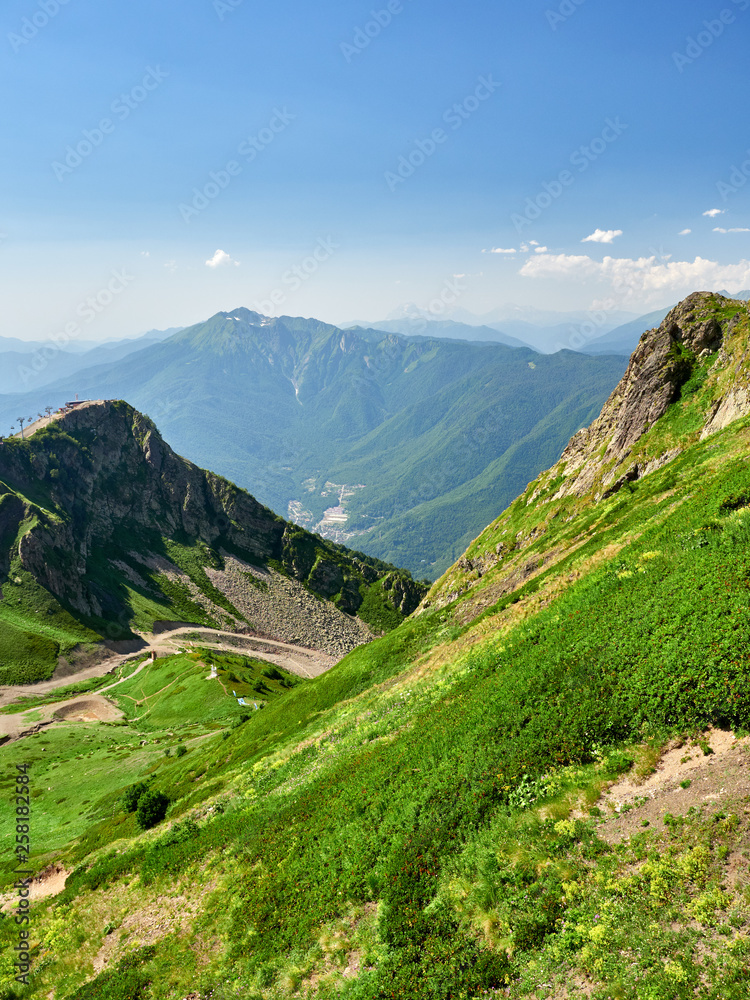 The peaks of a high mountain slope with cable car, in front of which is a valley with residential houses. The peaks of a high mountain slope with cable car, in front of which is a valley with residential houses.