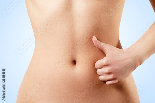 slim, athletic waist of a young woman on a blue background. The hand in the foreground shows a finger up gesture. the concept of female beauty and health, nutrition and diet, beautiful figure