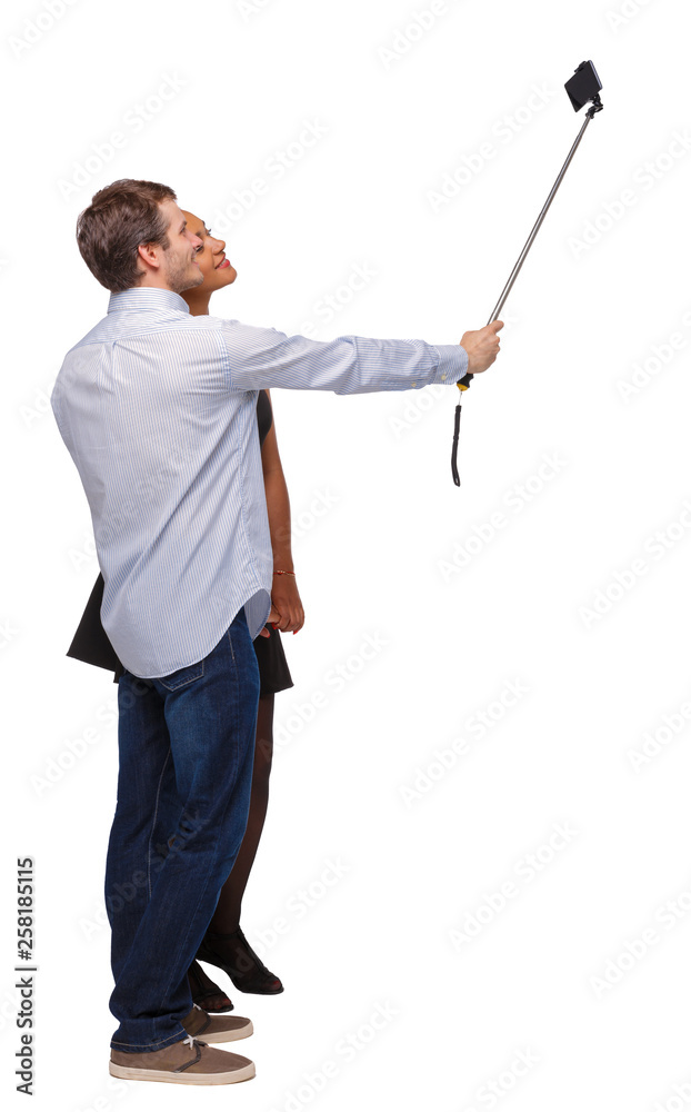 Back view of an interracial couple that makes selfie on selfie stick. Back view of an interracial couple that makes selfie on selfie stick.
