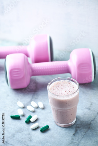 Glass of Protein Shake with milk and raspberries. BCAA amino acids, L - Carnitine capsules and pink dumbbells in background. Sport nutrition. Stone / Wooden background. Copy space.  photo