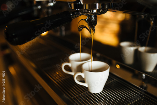 The moment of the brewing process of espresso. Coffee pours into two white cups.