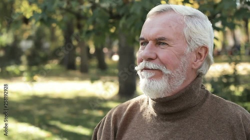 Attractive positive bearded senior man sittint outdoors. Elder male in good mood photo