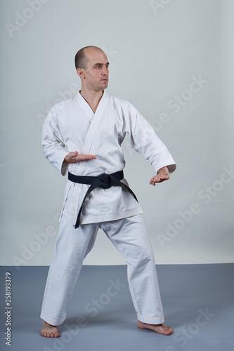 On a gray covering male athlete trains formal karate exercises