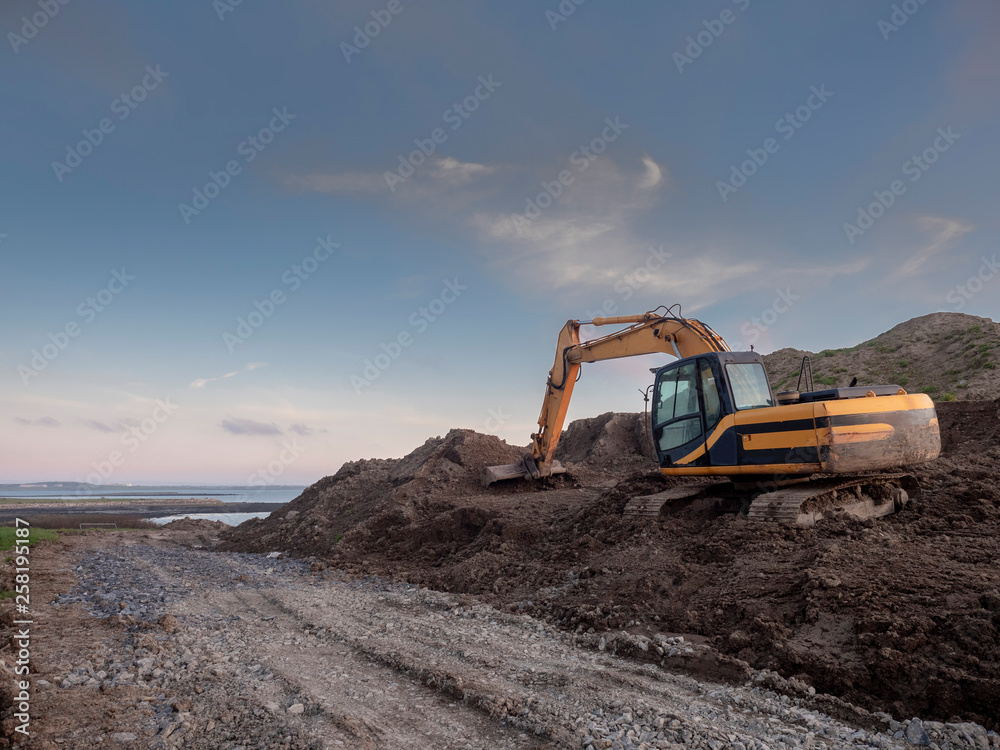 Digger working on a construction site, clean blue sky, Orange color of the digger.