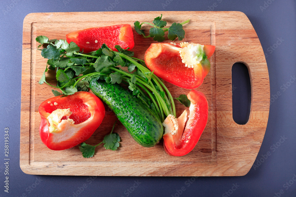 Red pepper, cucumber and greens on a wooden kitchen board, top view Red pepper, cucumber and greens on a wooden kitchen board, top view