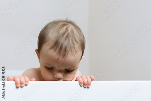 Baby girl thinking about something while standing in her crib.