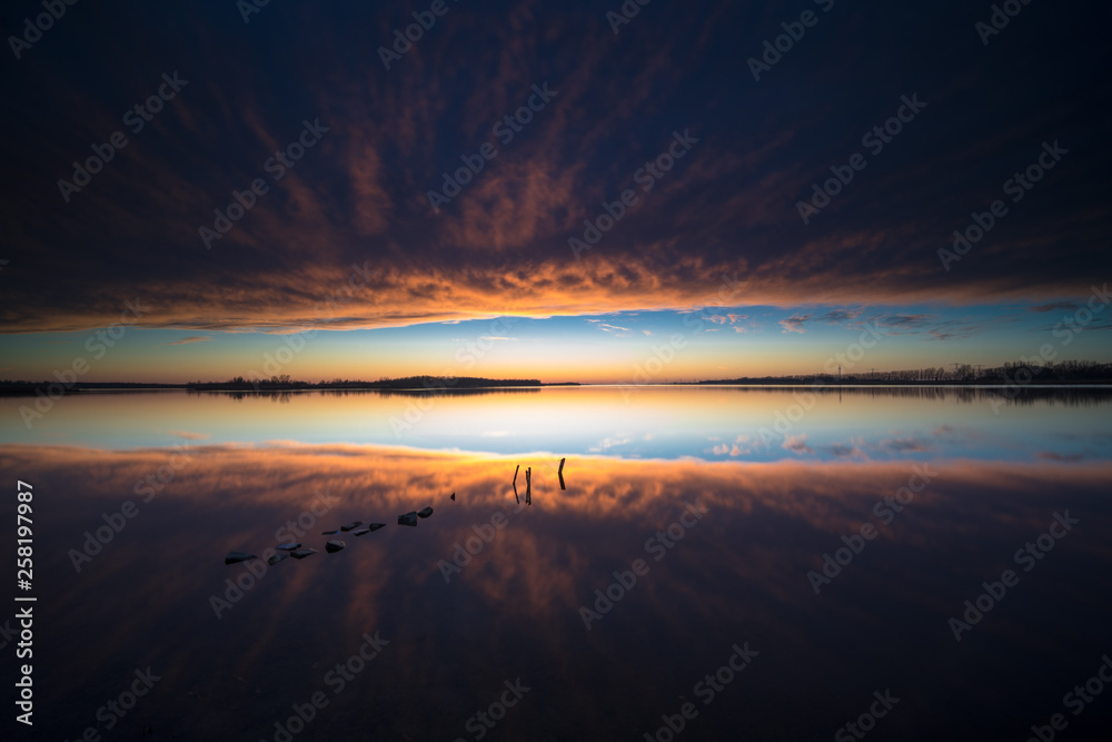 Atmospheric sunset above mirroring water surface with threatening clouds and an impressive landscape