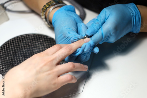 Hardware Manicure using electric device machine. procedure for the preparation of nails before applying nail polish. Hands of Manicurist in blue gloves and Nails of Client. Woman In Beauty Salon