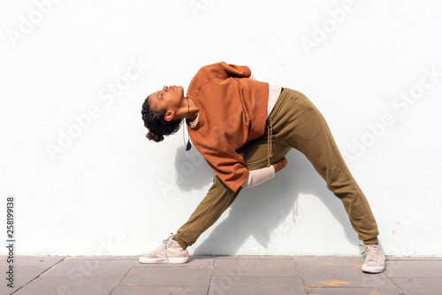 Stylish attractive young female runner in black sportswear doing warm-up routine outdoors before running against wall