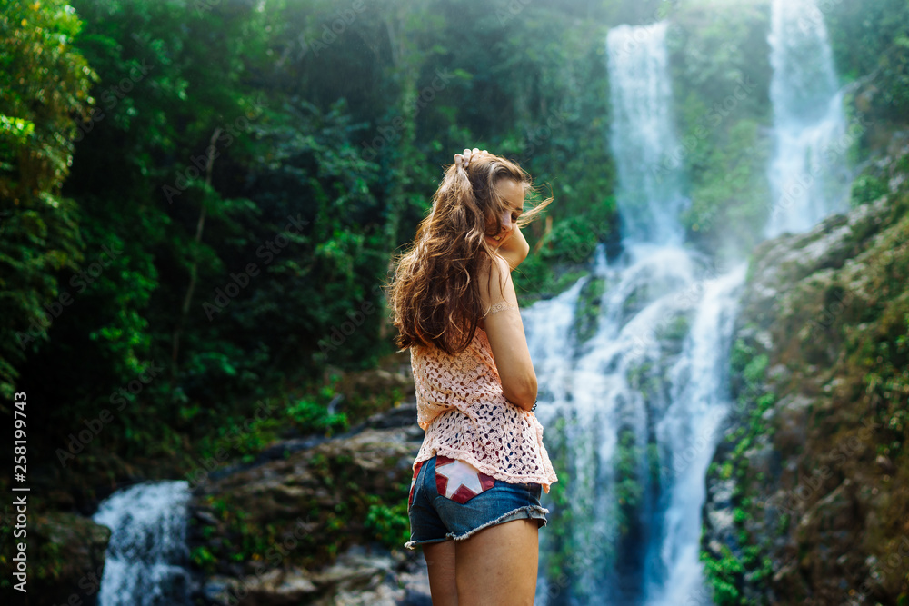 Young woman enjoying natural bathing by the Tamaraw waterfall on background. Puerto Galera, Mindoro Island, popular tourist place of Philippines