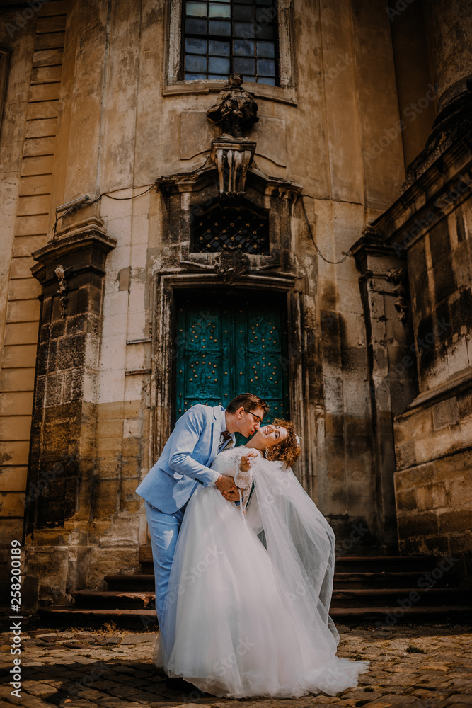 Naklejka premium Young beautiful couple bride and groom kisses each others on the background of the church