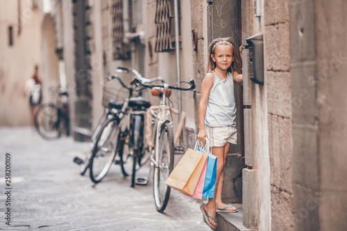 Portrait of adorable little girl walking with shopping bags outdoors in european city.